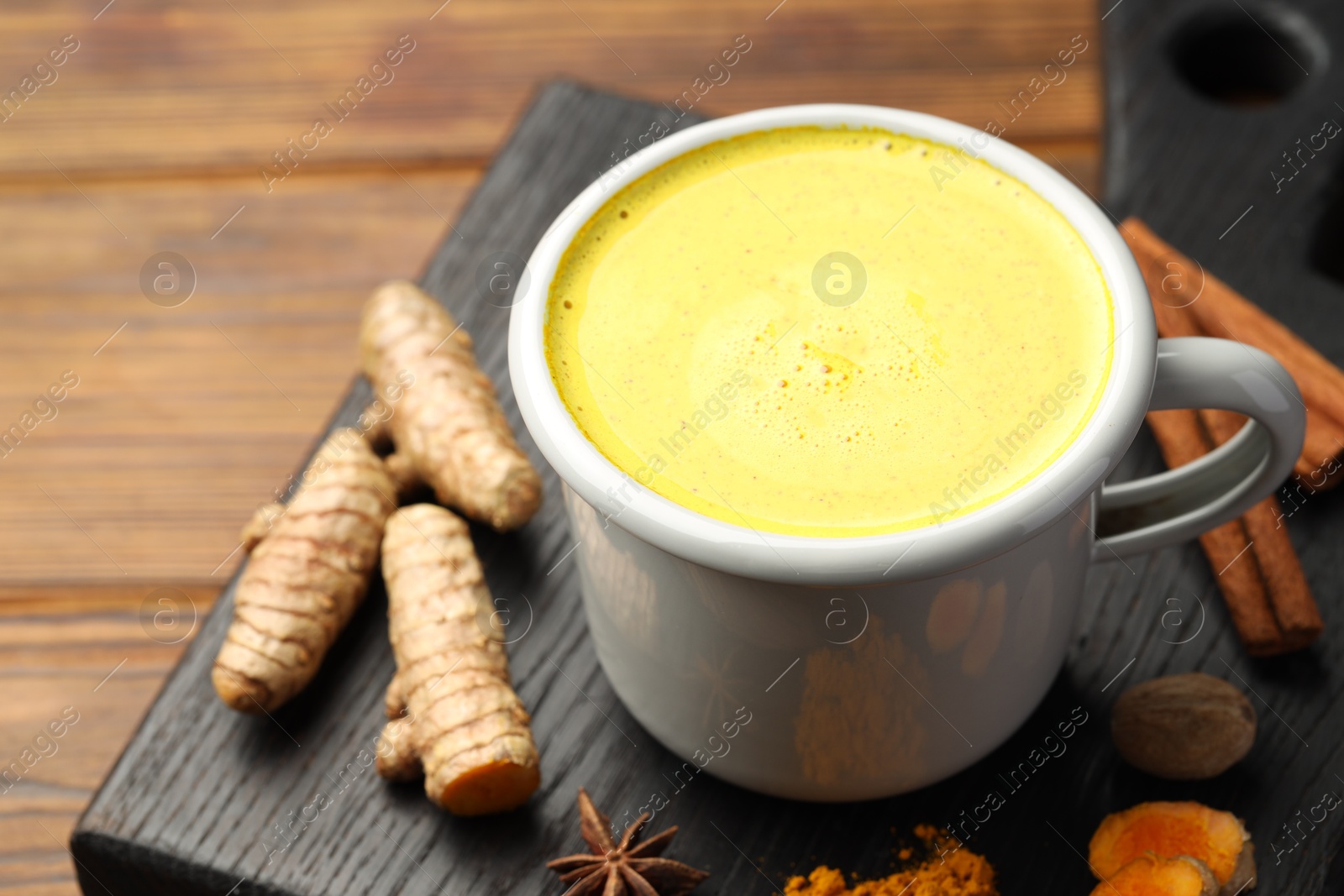 Photo of Tasty turmeric latte in cup and spices on wooden table, closeup