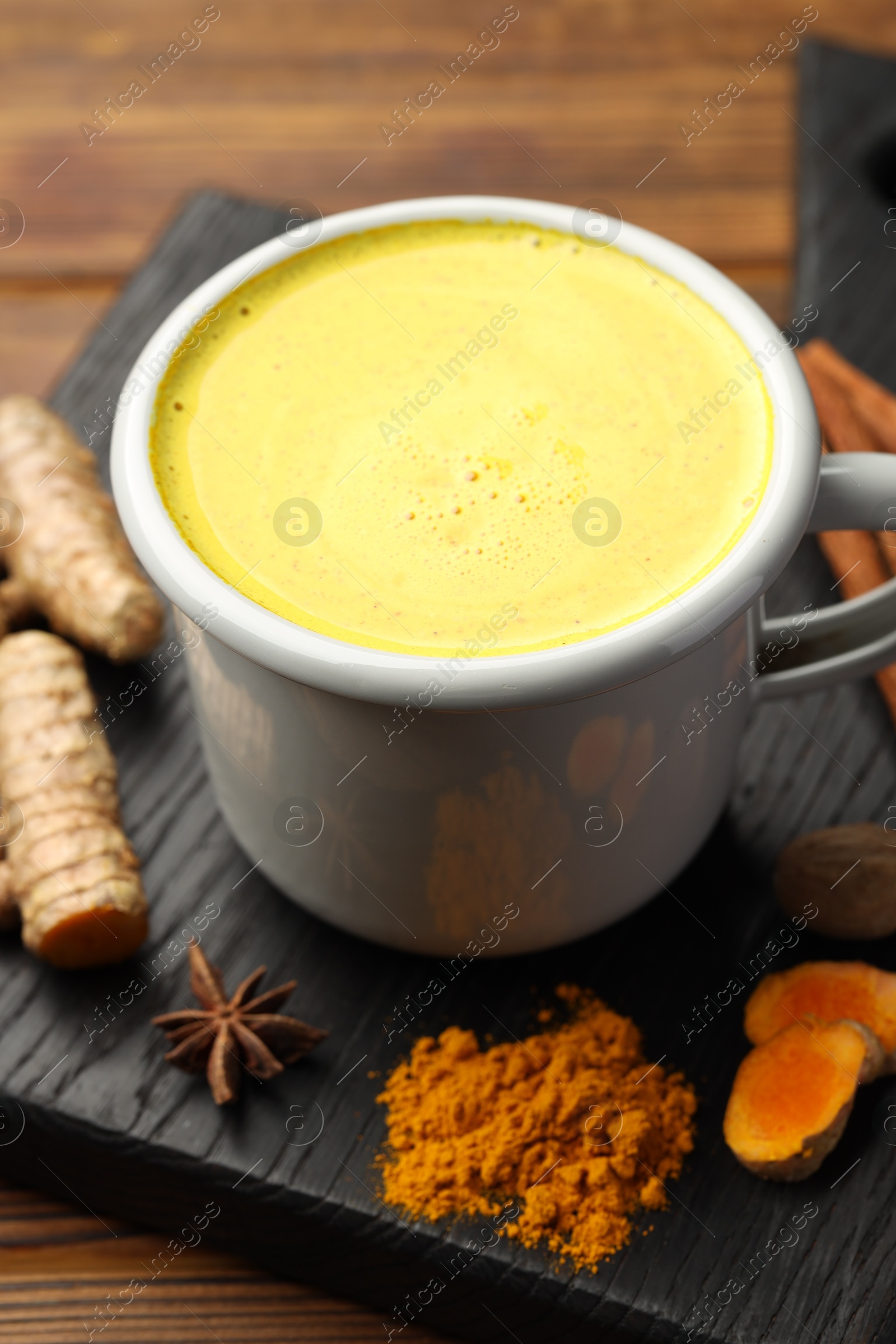 Photo of Tasty turmeric latte in cup and spices on wooden table, closeup