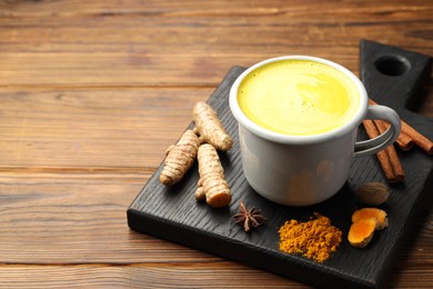 Photo of Tasty turmeric latte in cup and spices on wooden table, closeup. Space for text