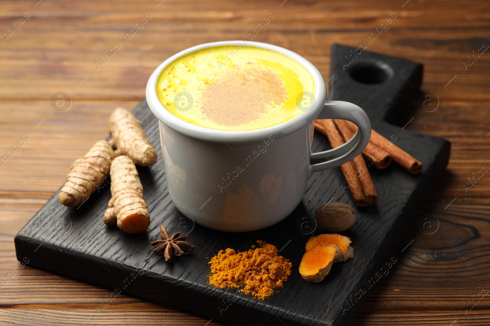 Photo of Tasty turmeric latte in cup and spices on wooden table, closeup