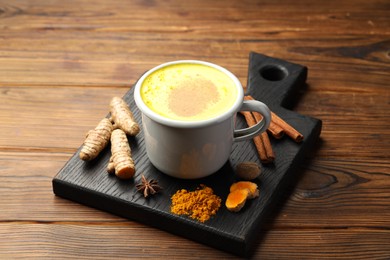 Photo of Tasty turmeric latte in cup and spices on wooden table