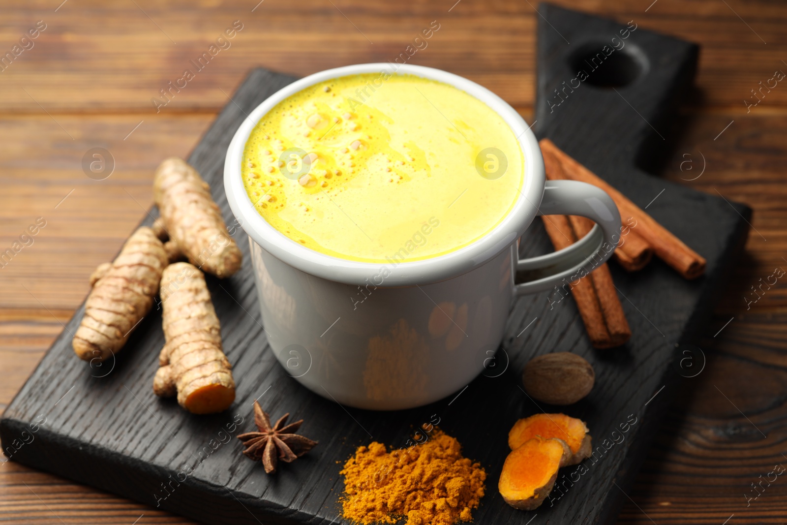 Photo of Tasty turmeric latte in cup and spices on wooden table, closeup