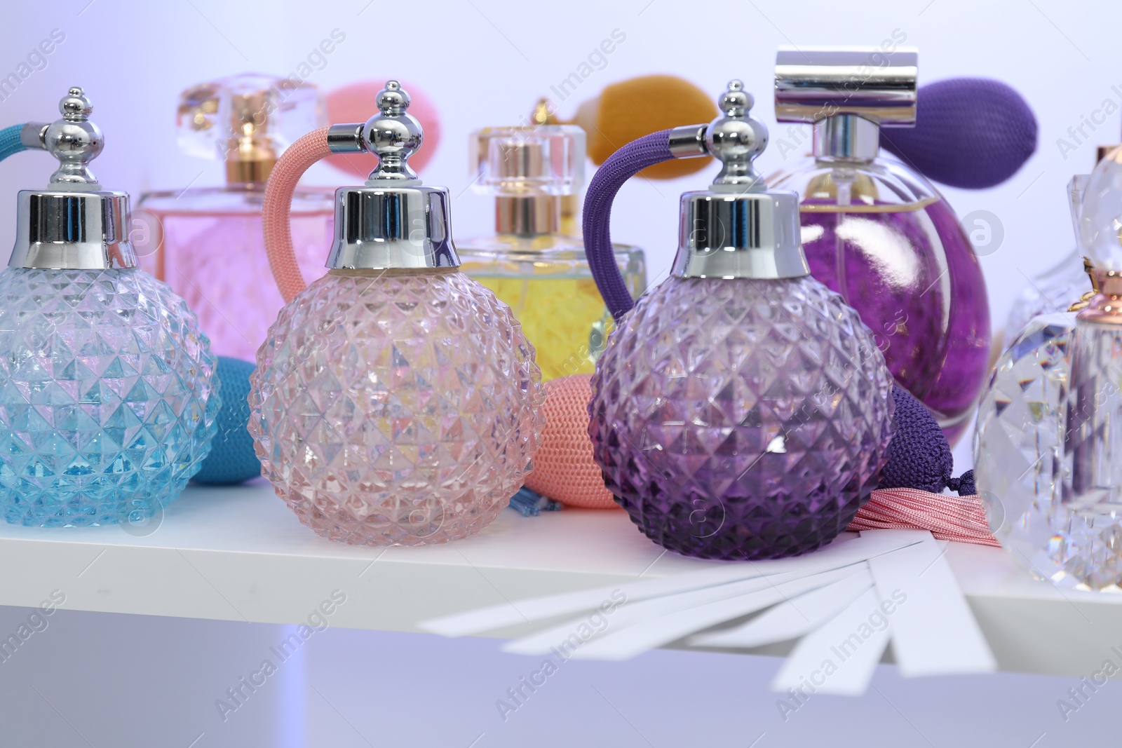 Photo of Different bottles of luxury perfume and fragrance blotters on shelf in store, closeup