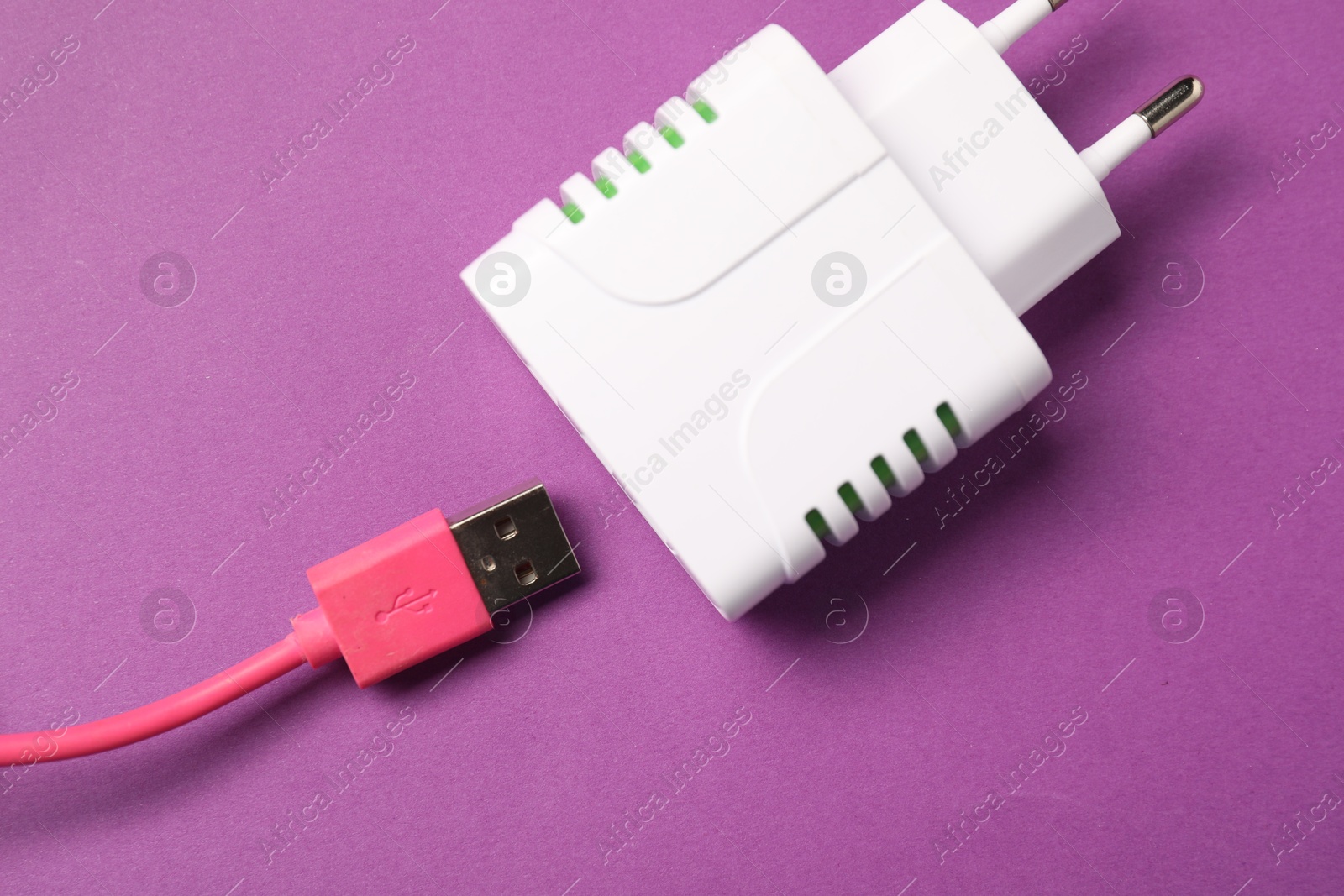 Photo of USB power adapter and charge cable on purple background, flat lay