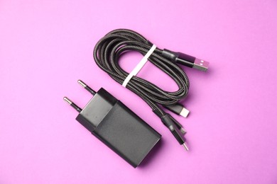 Photo of USB power adapter and triple charge cable on violet background, flat lay