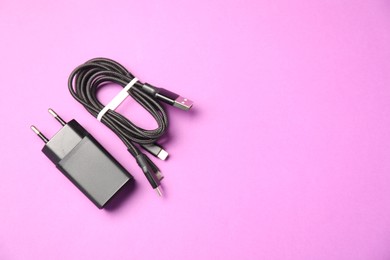 Photo of USB power adapter and triple charge cable on violet background, flat lay. Space for text