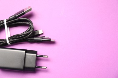 Photo of USB power adapter and triple charge cable on violet background, flat lay. Space for text