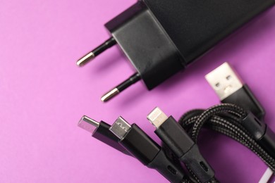 Photo of USB power adapter and triple charge cable on violet background, flat lay