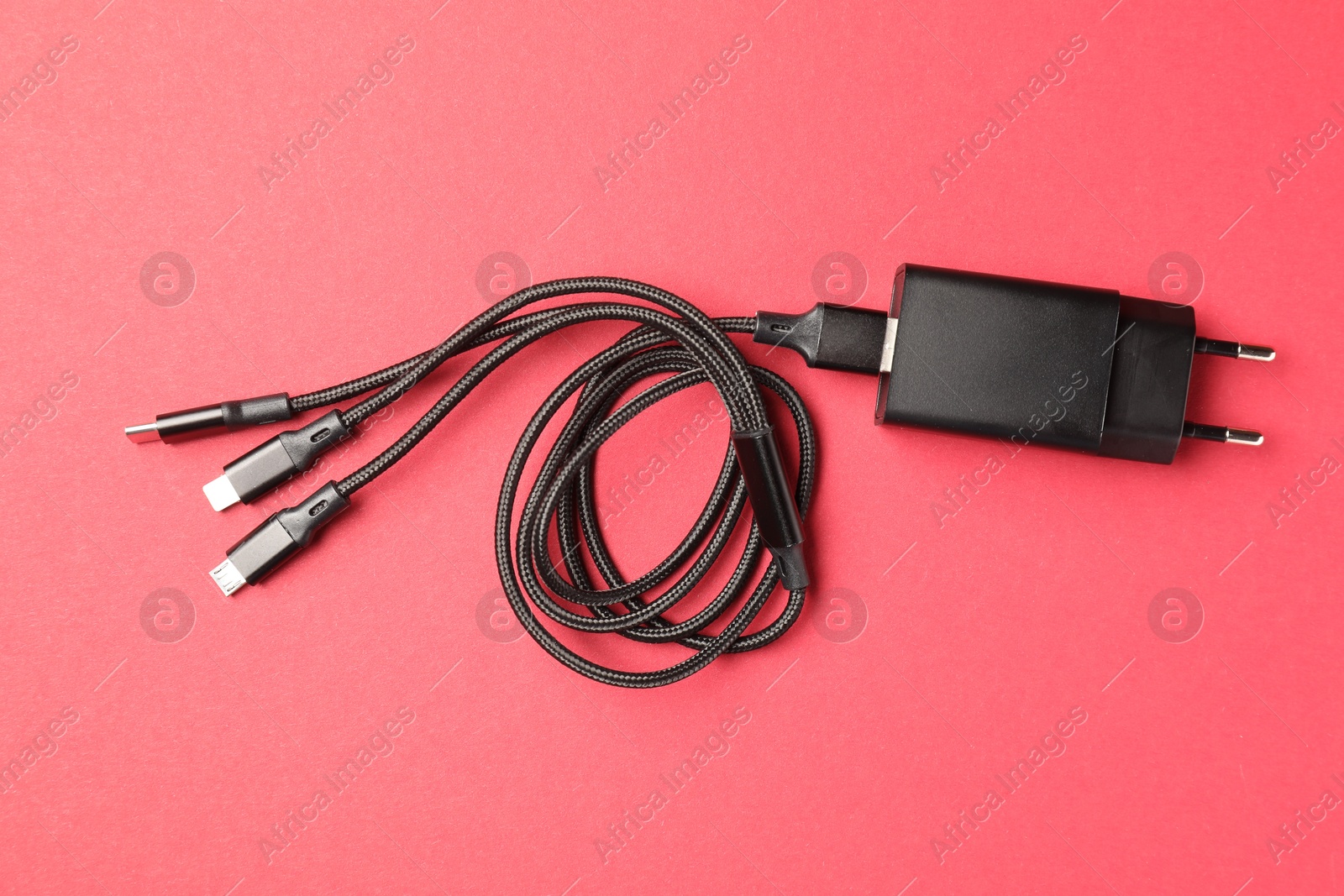 Photo of USB power adapter with triple charge cable on crimson background, top view