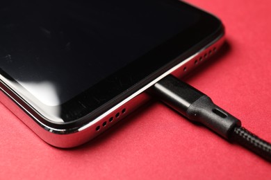 Photo of USB charge cable connected to smartphone on crimson background, closeup