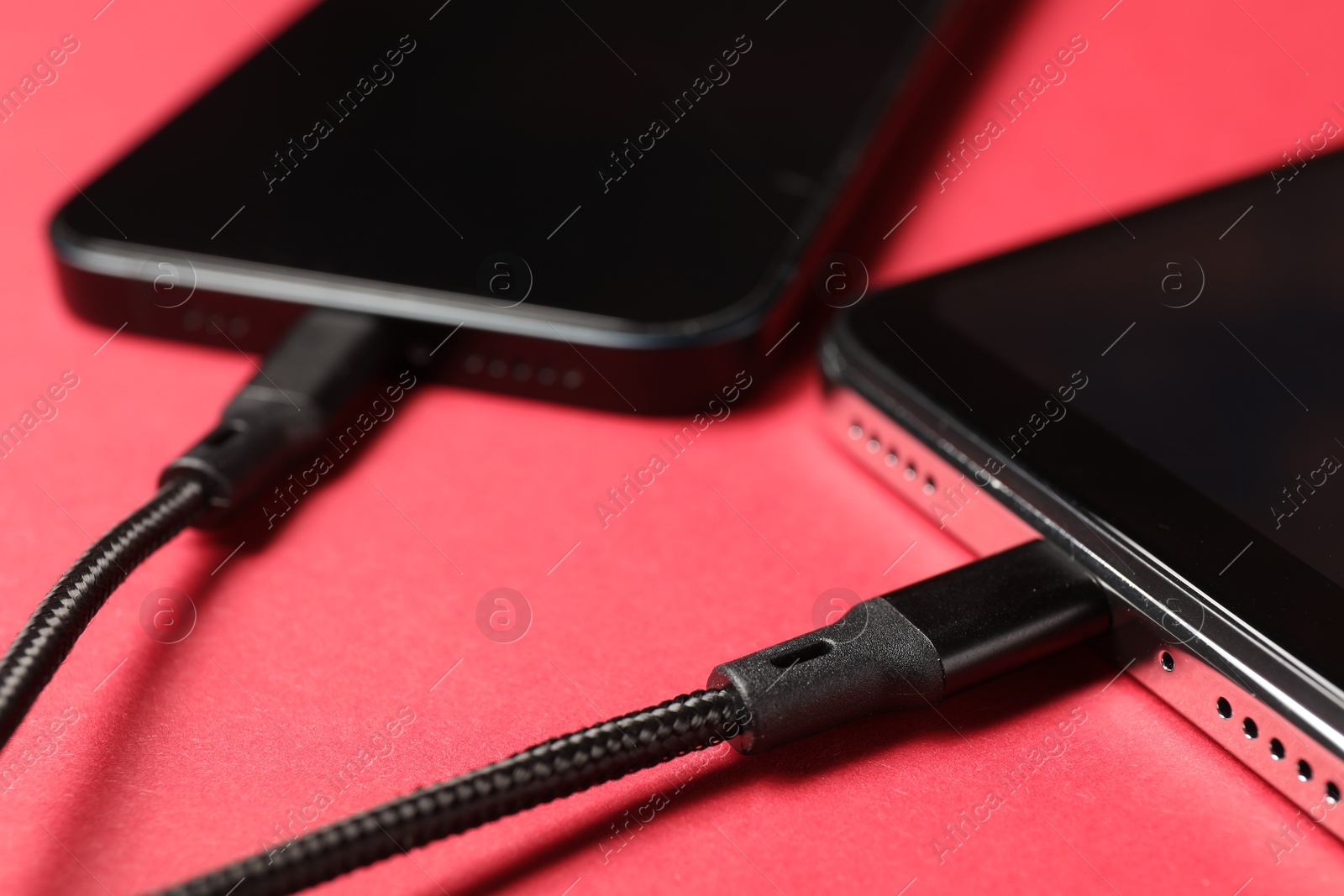 Photo of USB charge cables connected to smartphones on crimson background, closeup