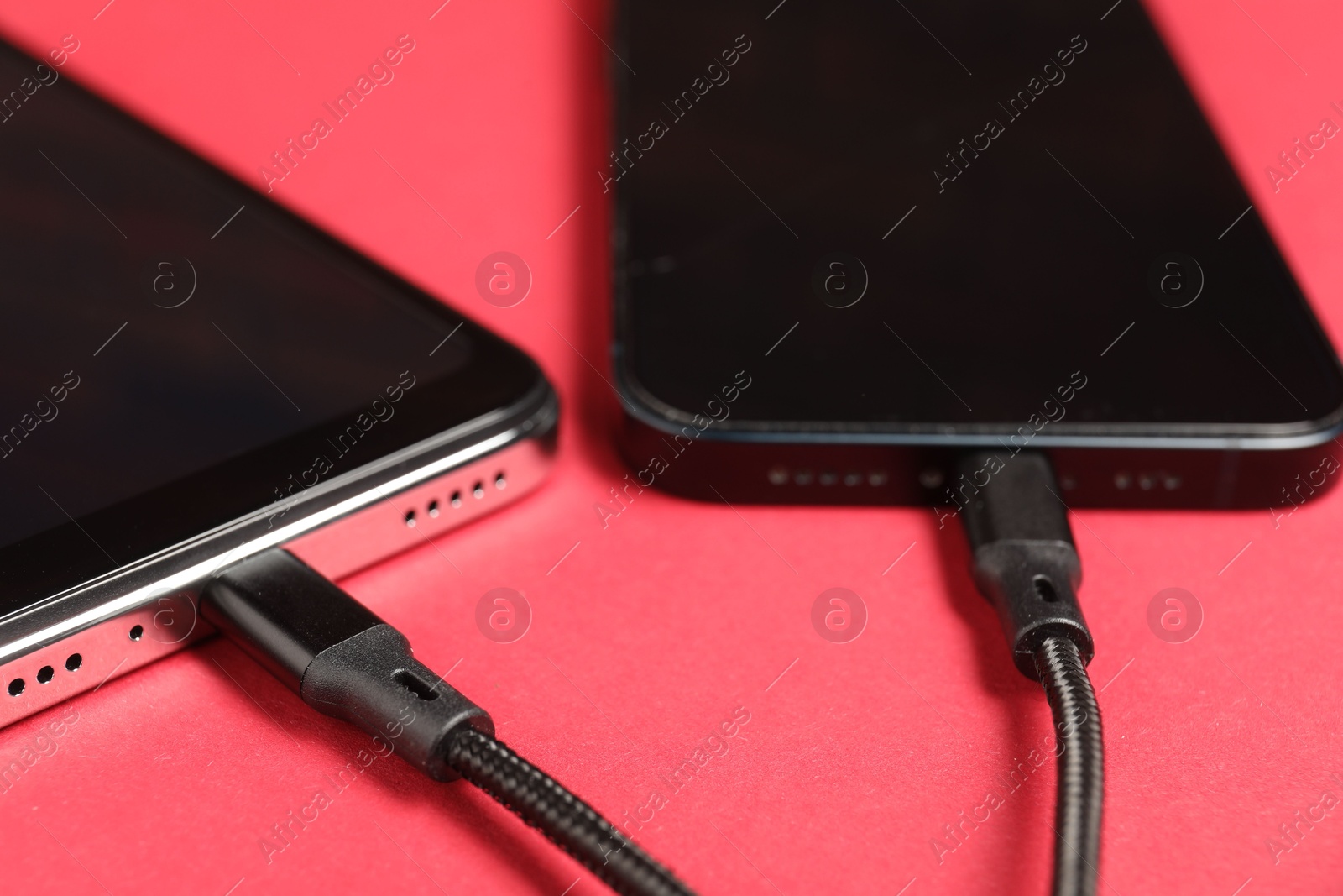 Photo of USB charge cables connected to smartphones on crimson background, closeup