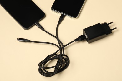 Photo of Triple charge cable connected to smartphones on beige background, above view