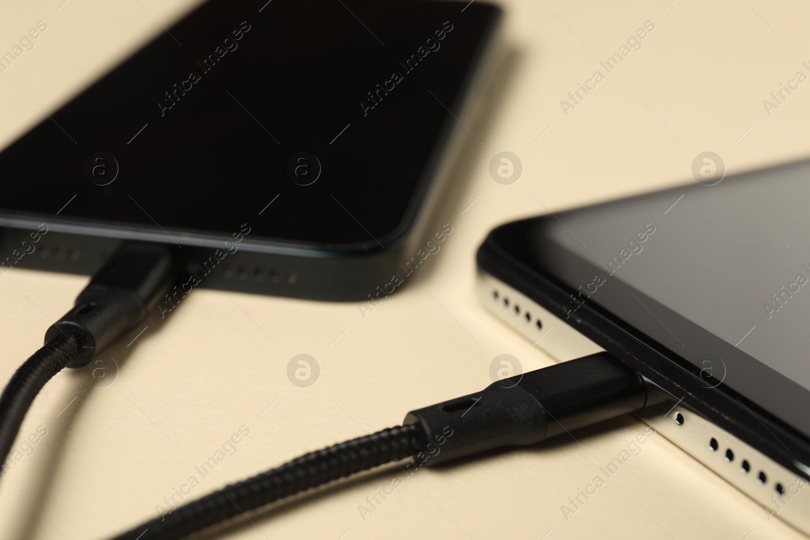 Photo of USB charge cables connected to smartphones on beige background, closeup