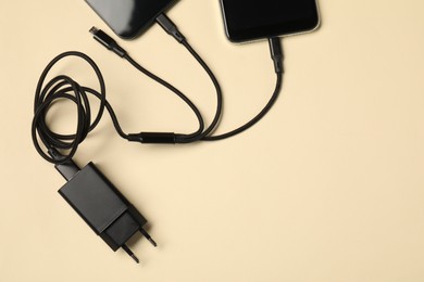 Photo of Triple charge cable connected to smartphones on beige background, flat lay. Space for text