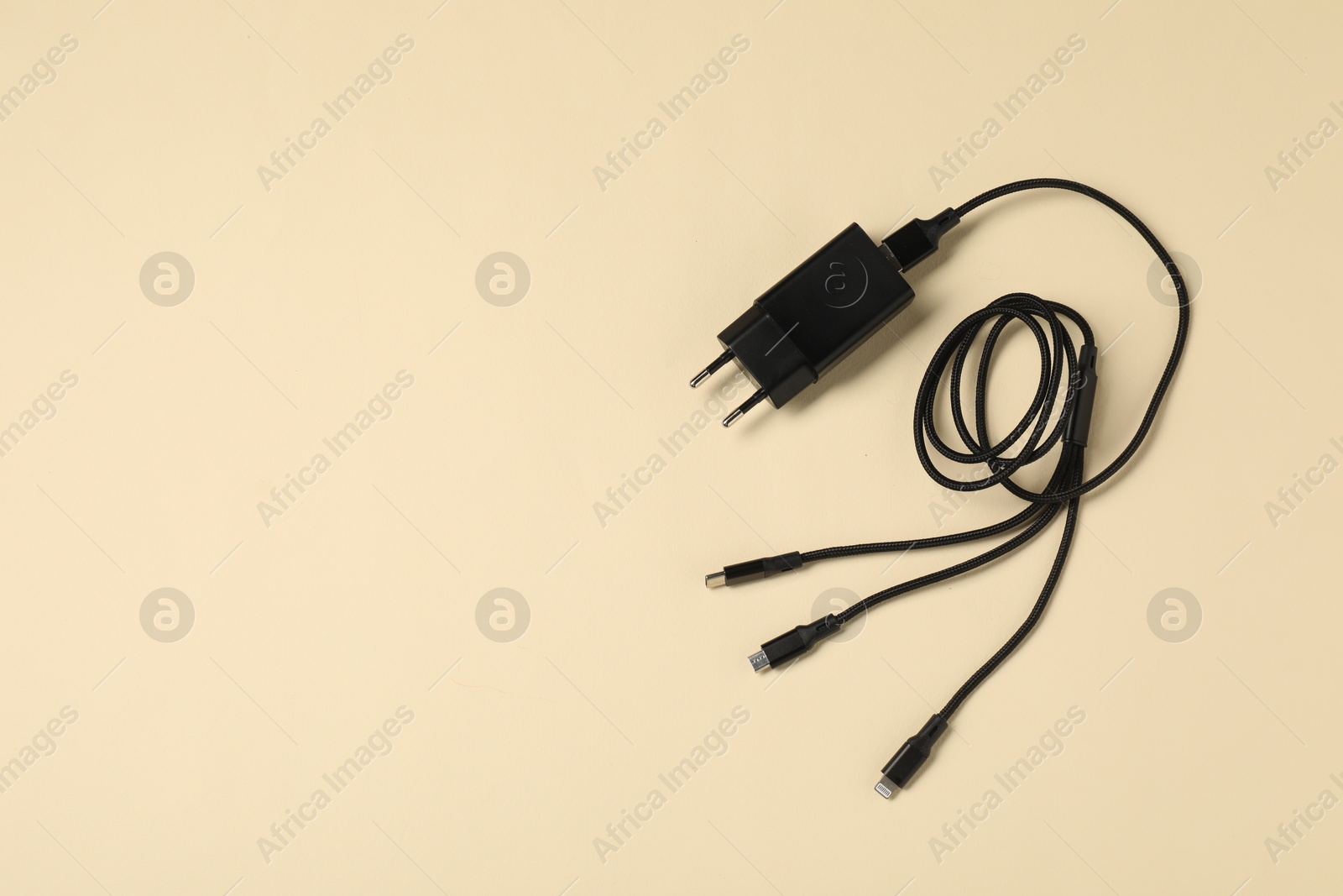 Photo of USB power adapter and triple charge cable on beige background, top view. Space for text