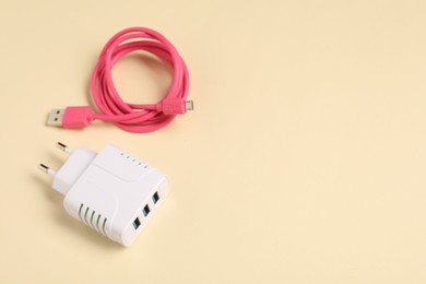 Photo of USB power adapter and charge cable on beige background, above view. Space for text