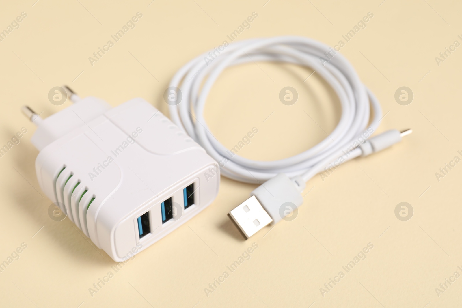 Photo of USB power adapter and charge cable on beige background, closeup