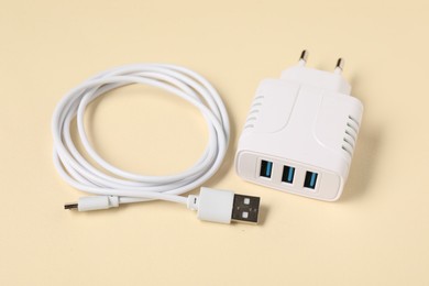 Photo of USB power adapter and charge cable on beige background, closeup