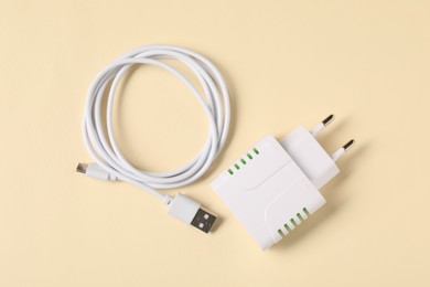 Photo of USB power adapter and charge cable on beige background, flat lay