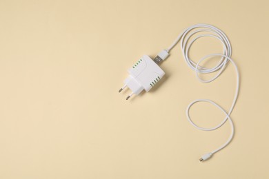 Photo of USB power adapter and charge cable on beige background, flat lay. Space for text