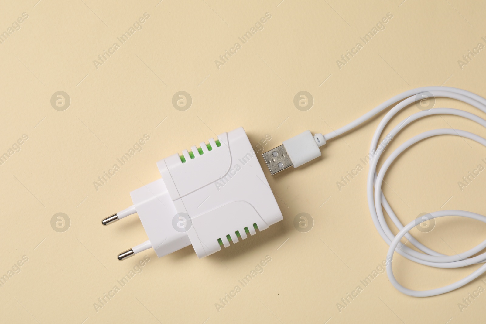 Photo of USB power adapter and charge cable on beige background, flat lay