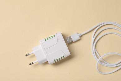 Photo of USB power adapter and charge cable on beige background, flat lay