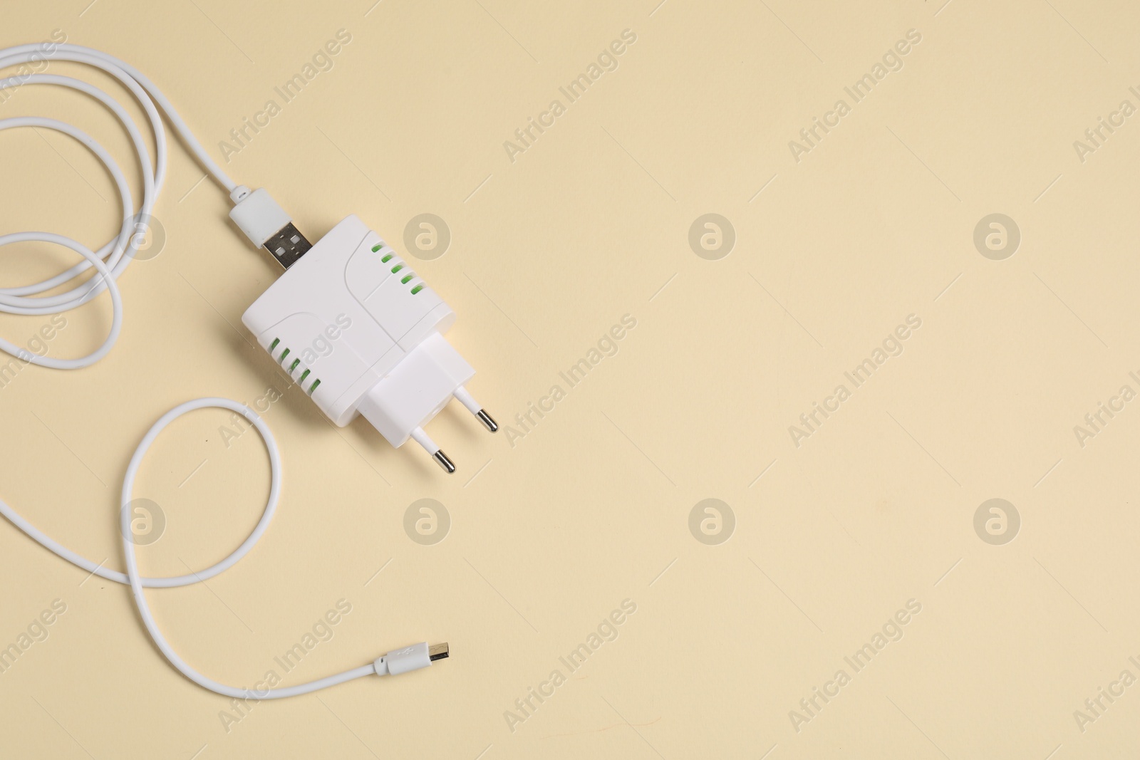 Photo of USB power adapter with charge cable on beige background, top view. Space for text