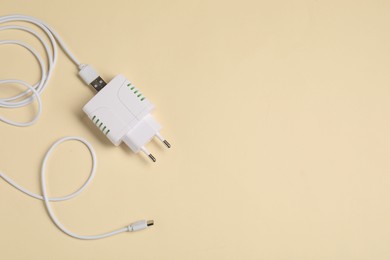 Photo of USB power adapter with charge cable on beige background, top view. Space for text