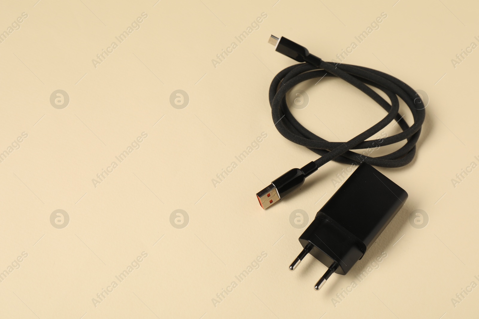 Photo of USB power adapter with charge cable on beige background, above view. Space for text