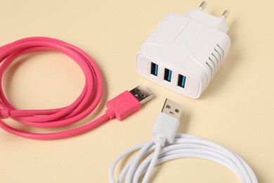 Photo of USB power adapter and charge cables on beige background, closeup