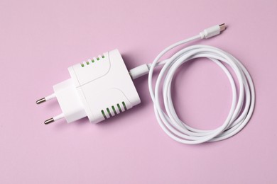 Photo of USB power adapter with charge cable on pink background, top view