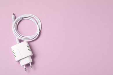 Photo of USB power adapter with charge cable on pink background, top view. Space for text