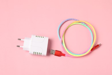 Photo of USB power adapter and charge cable on pale pink background, flat lay