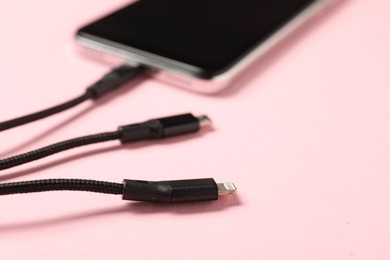 Photo of USB charge cable connected to smartphone on pale pink background, closeup. Space for text