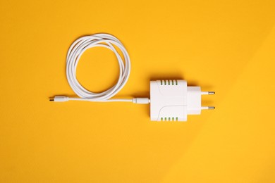 Photo of USB power adapter with charge cable on orange background, top view