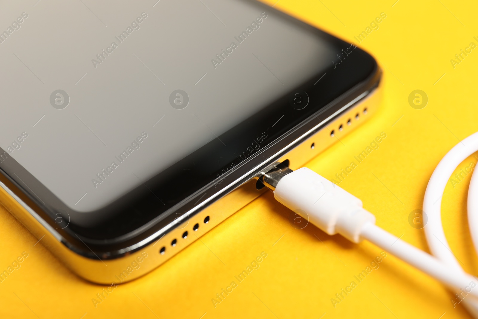 Photo of USB charge cable connected to smartphone on orange background, closeup