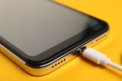 Photo of USB charge cable connected to smartphone on orange background, closeup