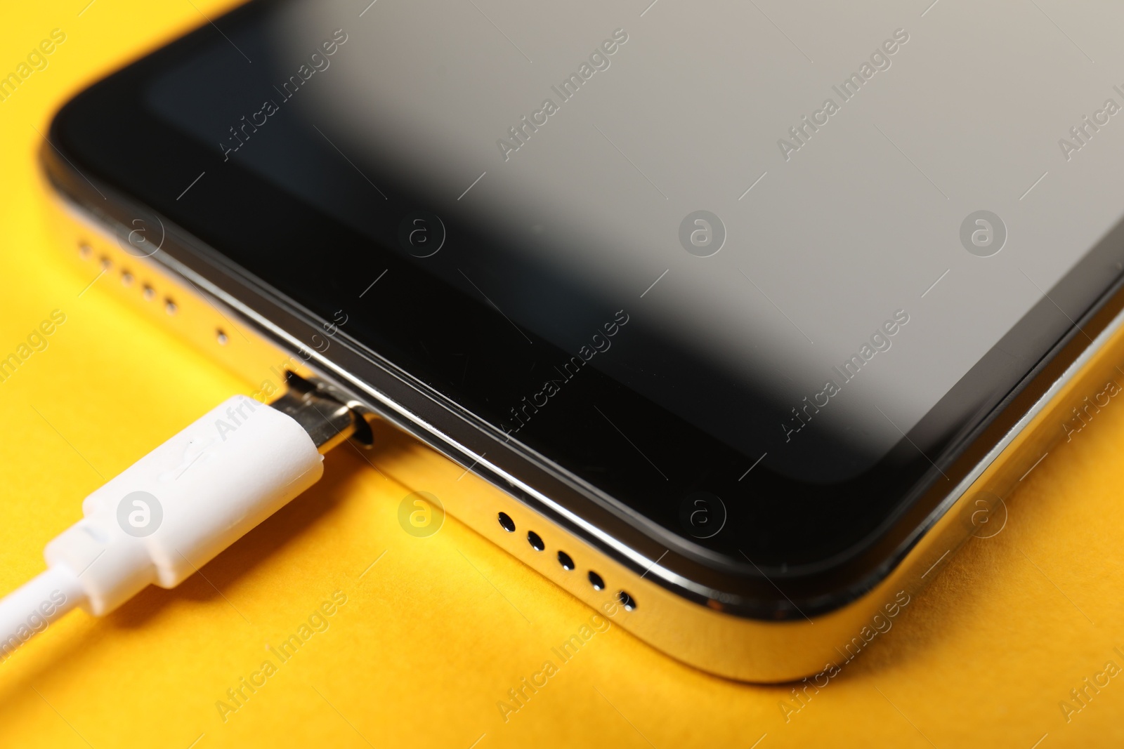 Photo of USB charge cable connected to smartphone on orange background, closeup