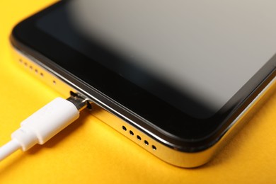 Photo of USB charge cable connected to smartphone on orange background, closeup