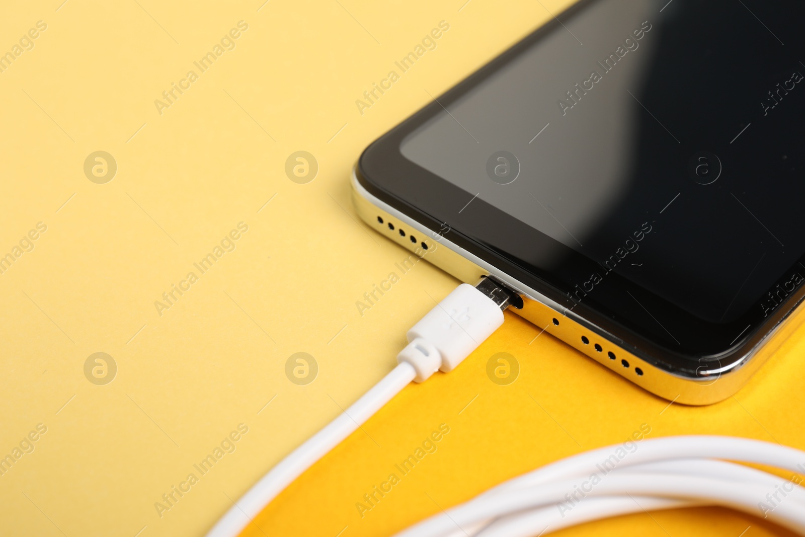 Photo of USB charge cable connected to smartphone on color background, closeup. Space for text