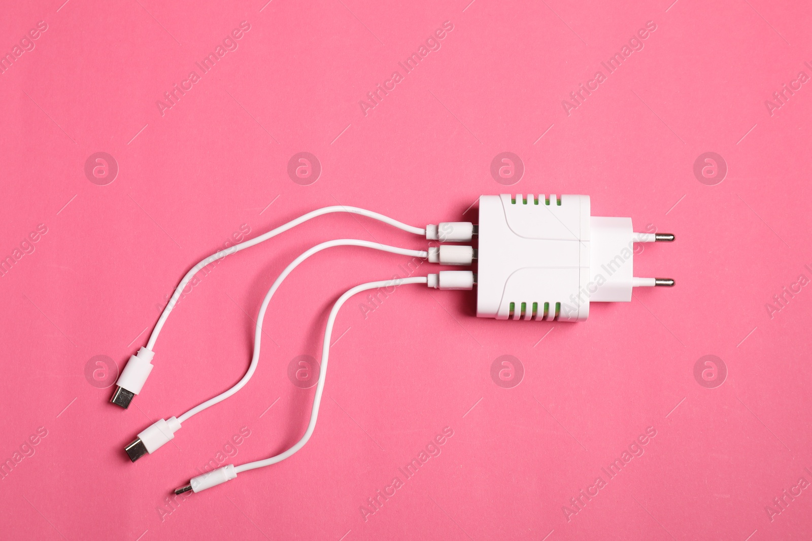 Photo of USB power adapter with charge cables on pink background, top view