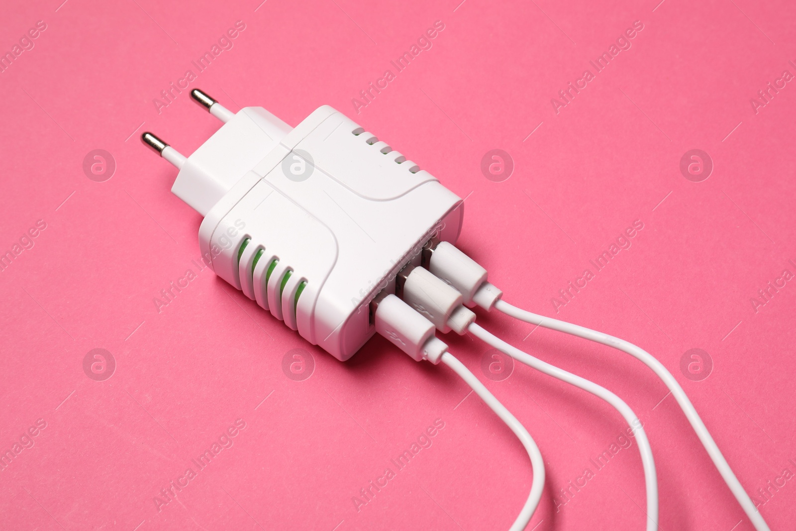 Photo of USB power adapter with charge cables on pink background, closeup