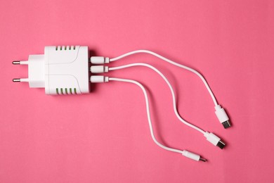 Photo of USB power adapter with charge cables on pink background, top view