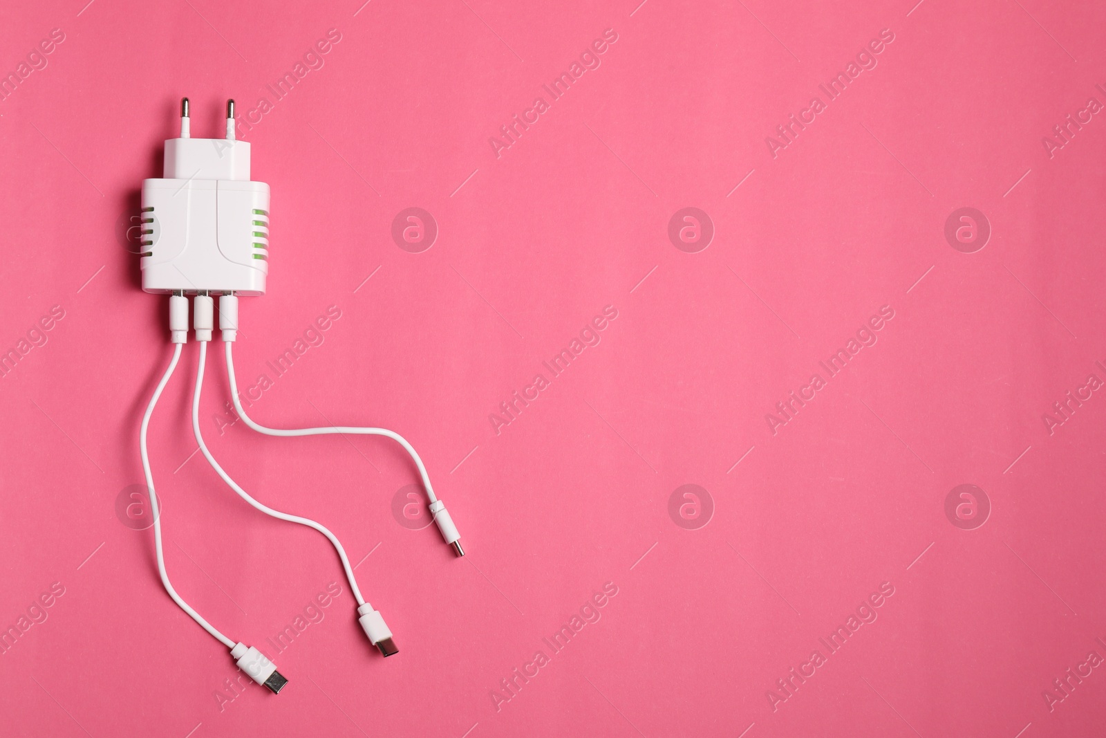 Photo of USB power adapter with charge cables on pink background, top view. Space for text