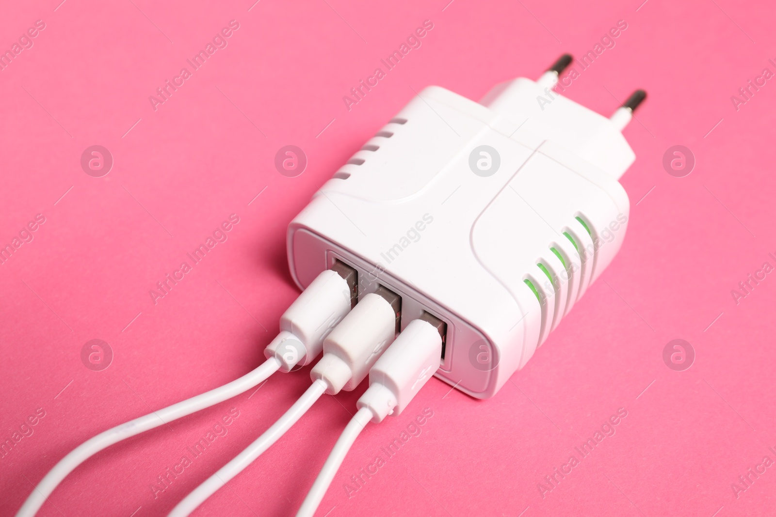 Photo of USB power adapter with charge cables on pink background, closeup