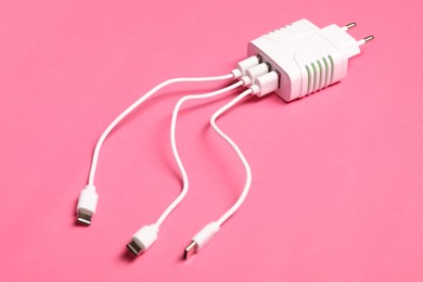 Photo of USB power adapter with charge cables on pink background, closeup