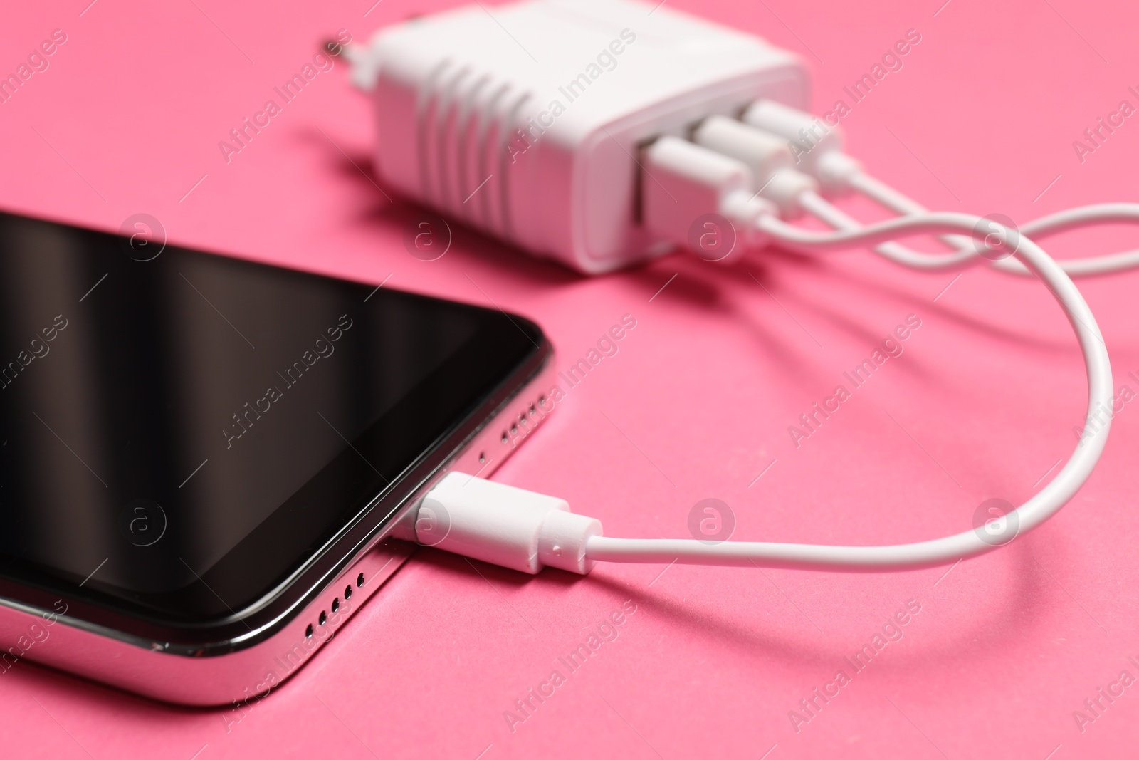 Photo of USB charge cable connected to smartphone on pink background, closeup