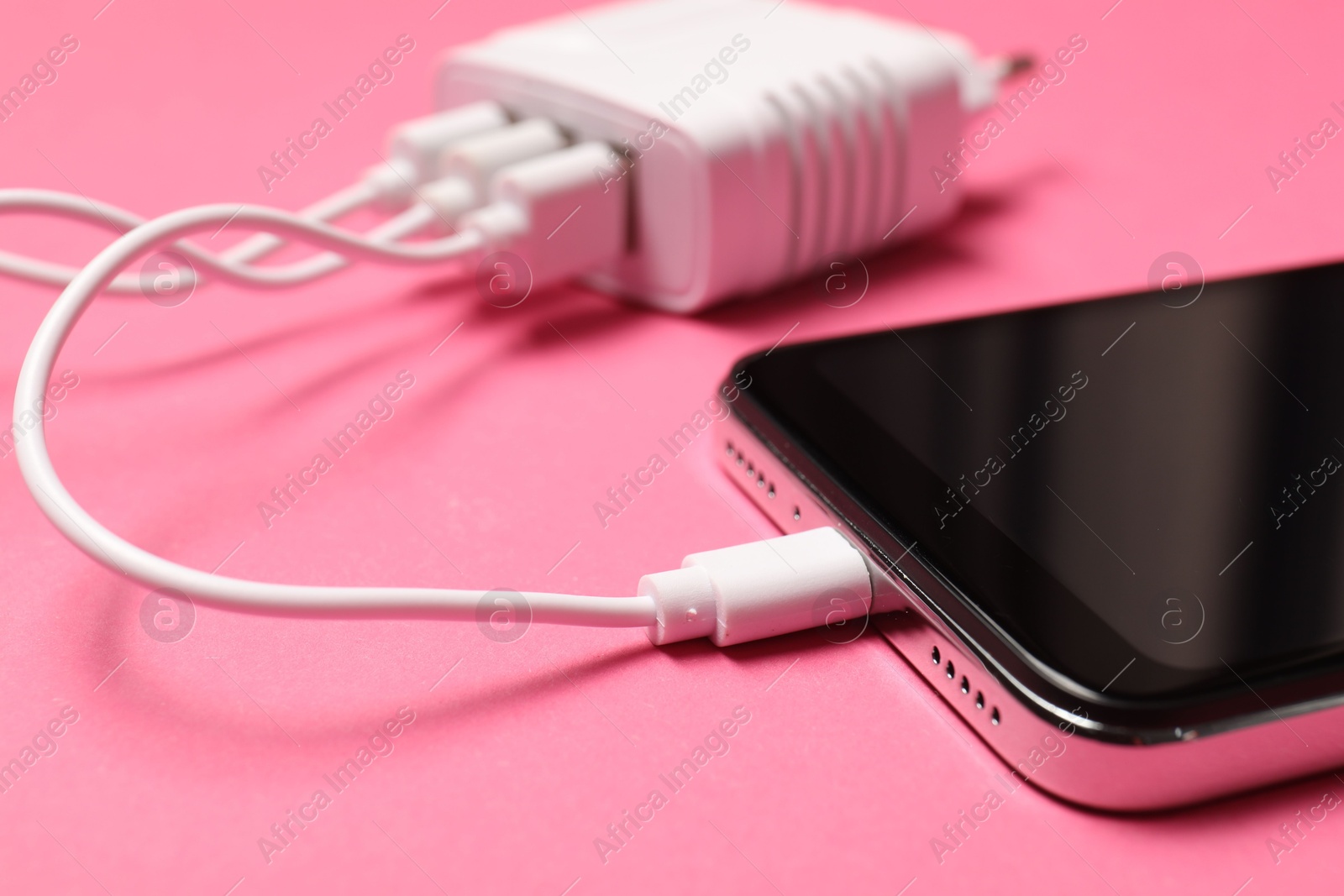 Photo of USB charge cable connected to smartphone on pink background, closeup