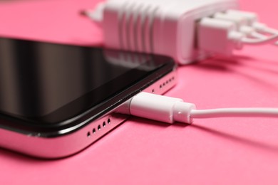 Photo of USB charge cable connected to smartphone on pink background, closeup